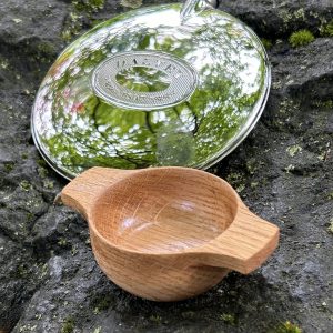 Handcrafted individual oak dram quaich set alongside Dalvey hip flask on rock