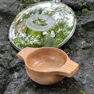 Handcrafted individual oak dram quaich set alongside Dalvey hip flask on rock